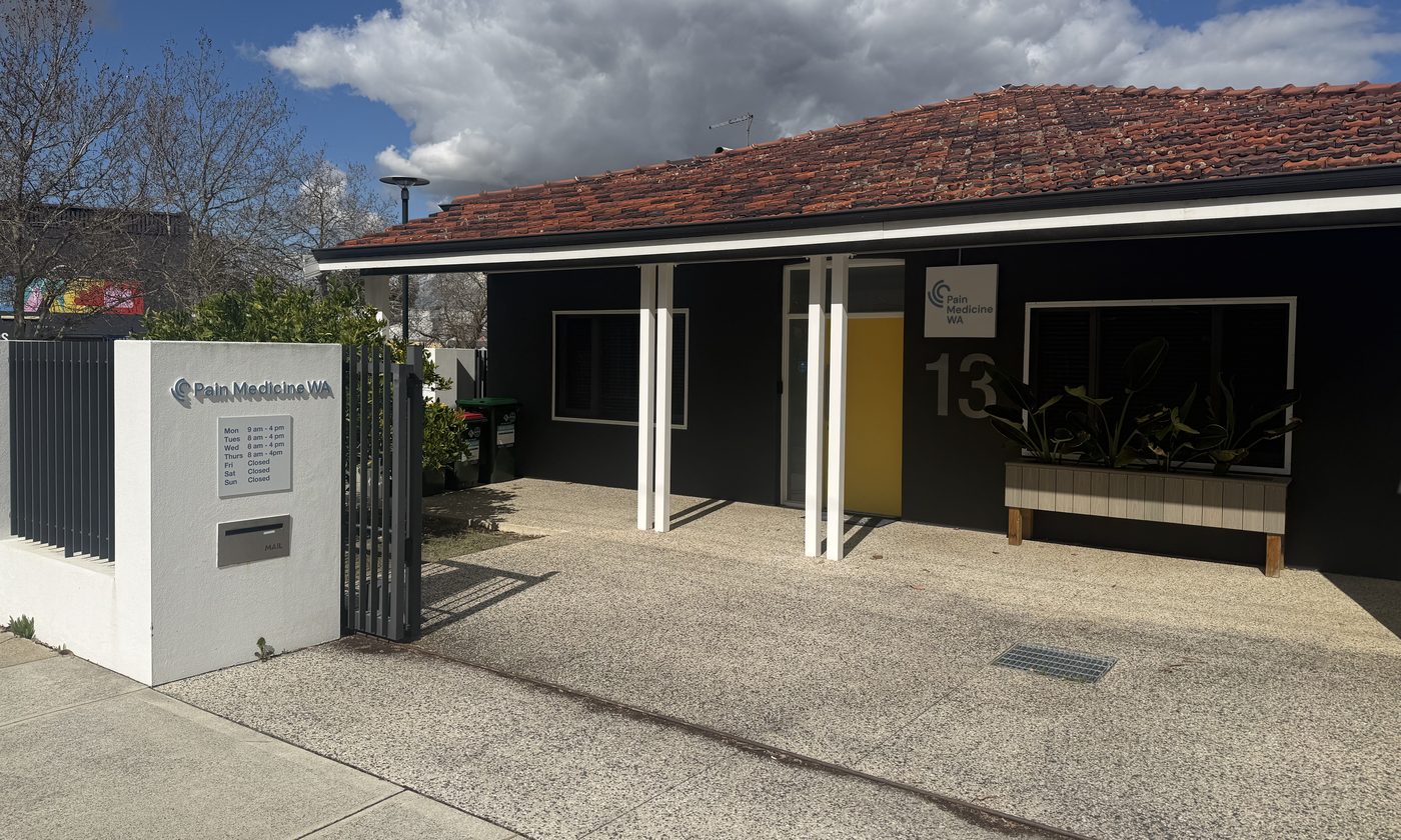 Entrance to Pain Medicine WA at 13 Grosvenor Road, Mount Lawley — a dark building with a yellow front door, the practice sign and consulting hours at the front gate